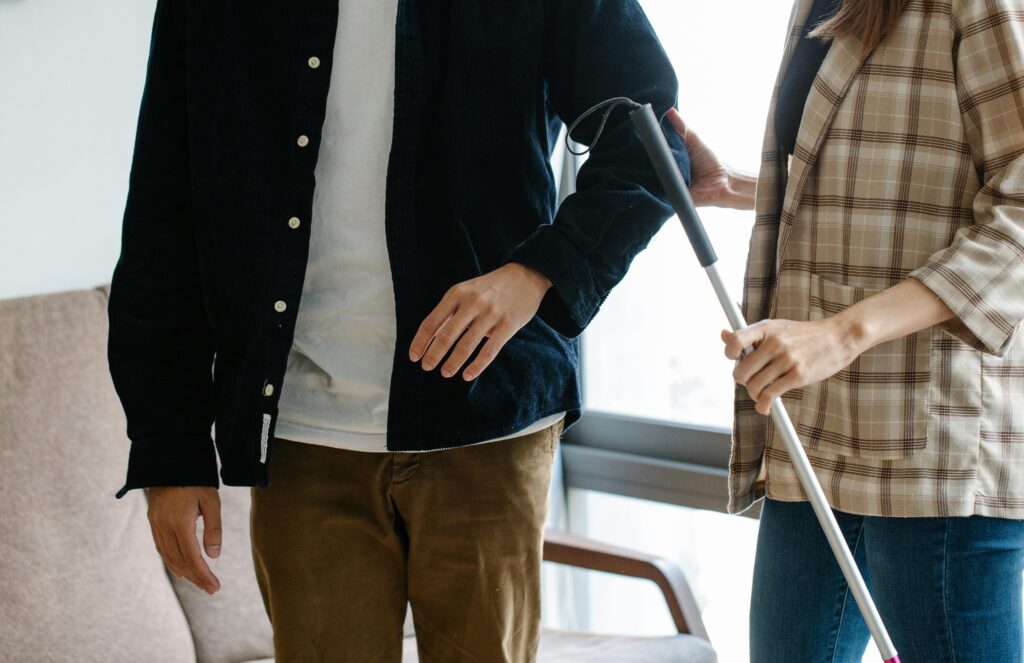 pexels photo 7188859 7188859 Two adults providing support indoors with a walking stick, displaying teamwork and care.
